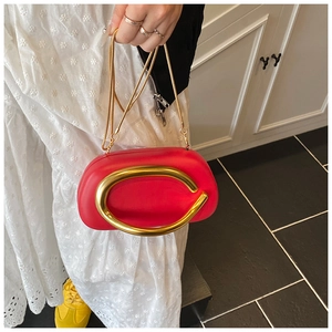 Detail of red oval clutch bag with large gold C-shaped metal clasp and snake chain