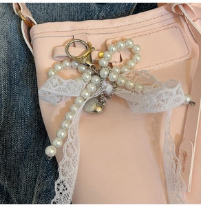 Detail of a sweet lace bow charm with white pearls and heart pendant on a pink bag