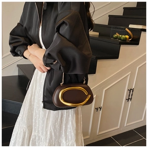 Detail of dark brown leather clutch featuring a large gold C-shaped metal ornament