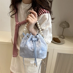 Blue drawstring bucket bag with floral embroidery, butterfly detail, and pearl handle