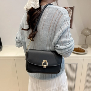 Sac sous le bras minimaliste en cuir noir avec boucle dorée porté par un modèle