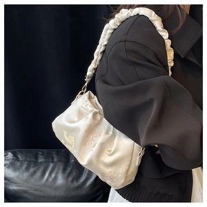 Detail of cream pleated satin shoulder bag with delicate floral print on a model