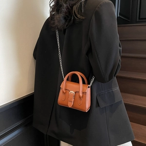 Brown mini crossbody bag with silver chain strap shown on model in modern interior