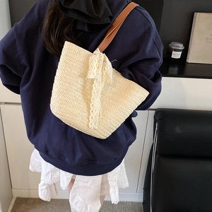 Large beige woven straw tote bag with white lace bow and brown leather strap