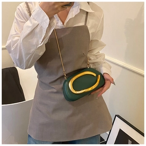 Close-up of dark green leather crossbody bag with bold gold buckle on white shirt