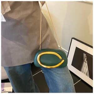 Detailed shot of dark green leather bag with large C-shaped gold buckle and chain strap