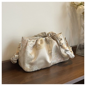 Close-up of beige pleated shoulder bag with floral patterns and gold chain hardware