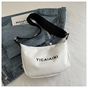 Macro view of white canvas crossbody bag with adjustable strap on denim jacket