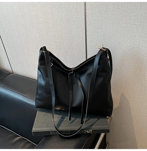 Detailansicht einer schwarzen Leder-Tragetasche mit minimalistischer V-Kurve auf einem Buch