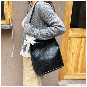 Detail of black pleated leather tote bag with a white lace bow charm hanging on the side