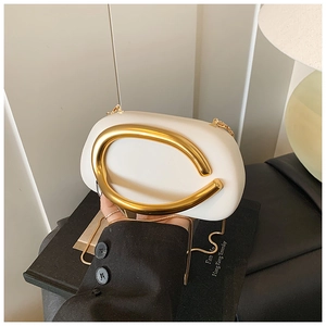 Detail of white minimalist clutch featuring a large gold C-shaped metal handle and chain