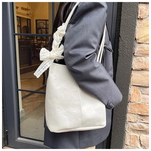 Detailed texture of white leather shoulder bag with elegant lace bow on strap worn by model