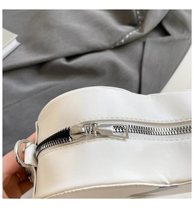 Détail du zip argenté et de l'anneau en D sur sac en cuir blanc avec motif éclair