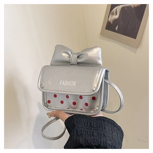 Detail of silver crossbody bag featuring a large metallic bow and red polka dot pattern