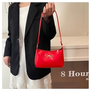 Detailed view of red leather shoulder bag with elegant gold metal bow decoration