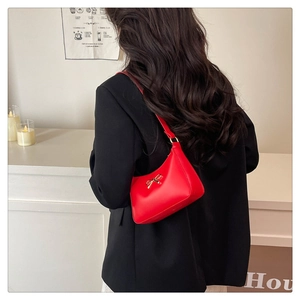 Detail of red leather shoulder bag featuring a gold bow clasp on a minimalist design