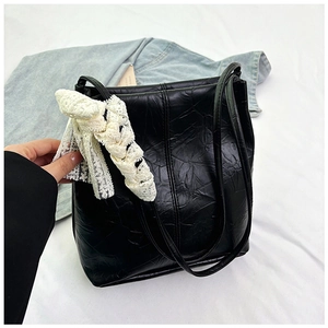 Detail of black pleated faux leather tote bag with elegant white lace bow decoration