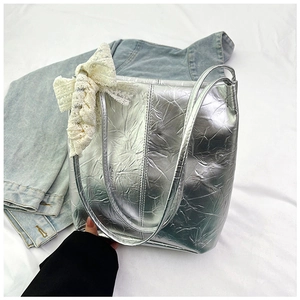 Detail of silver metallic pleated tote bag featuring a delicate white lace bow accessory