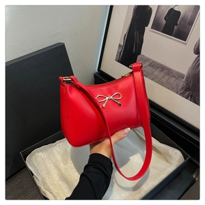 Detail of red shoulder bag featuring a golden bow decoration in a premium gift box