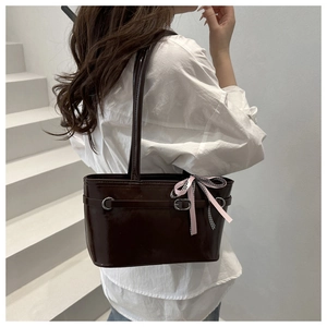 Detail of dark brown glossy patent leather tote with decorative ribbon bow on shoulder strap