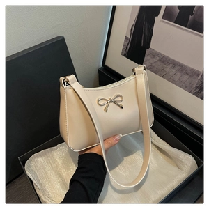 Detailed close-up of golden bow hardware on a cream leather hobo bag inside a gift box