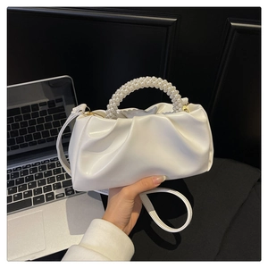 Detail showing white pleated cloud bag with pearl handle and golden hardware accents