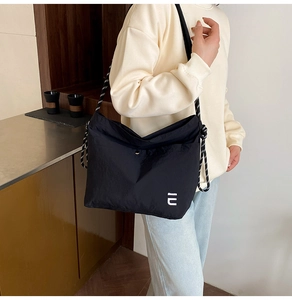 Détail du sac bandoulière en nylon noir avec sangle à carreaux et logo blanc décoratif