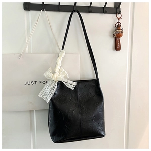 Detail of a black faux leather bucket bag featuring a white lace bow and pleated texture