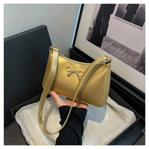 Close-up of golden metallic bow detail and texture on a stylish underarm bag