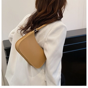 Model wearing a camel brown leather shoulder bag with a textured pebble finish and silver buckle