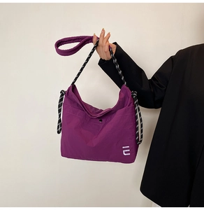 Detailed close-up of a purple crescent shoulder bag with woven rope strap and metal snap closure
