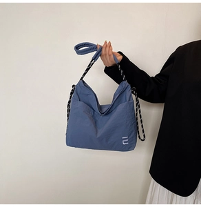 Close-up of blue nylon crossbody bag with woven strap and embroidered logo detail