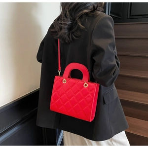 Detail of red quilted leather bag showing gold hardware and stitching on a black blazer