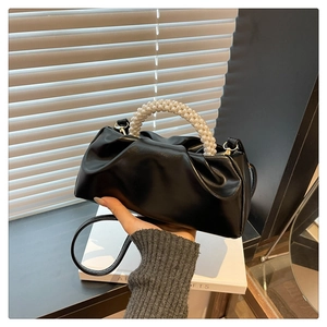 Detail of black pleated cloud bag featuring a large pearl bead top handle and leather strap