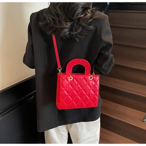Detail of red quilted PU leather handbag featuring a half-round handle and gold metal clips