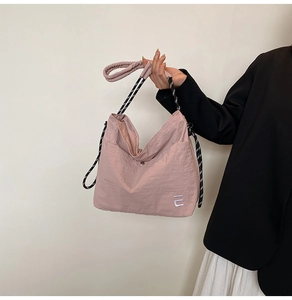 Detail of pink nylon tote bag featuring white embroidery and striped rope shoulder strap