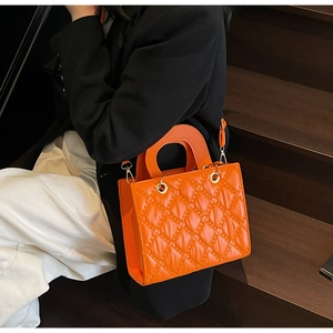 Detail of bright orange quilted handbag with glossy finish and gold metal hardware accents