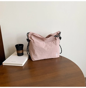 Détail du sac en nylon rose clair avec logo blanc et bandoulière corde sur table bois