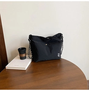 Détail du sac bandoulière en nylon noir avec sangle tissée sur table en bois