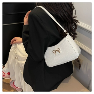 Sac à bandoulière blanc effet crocodile avec nœud doré porté par un mannequin de côté