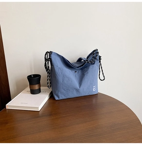 Détail du sac bandoulière en nylon bleu avec poignées tressées et logo U blanc gravé