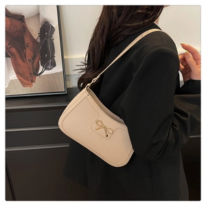 Close-up of beige crocodile pattern leather bag featuring a gold bow metal buckle detail