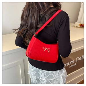 Detail of red crocodile texture underarm bag featuring a golden metal bow and slim strap