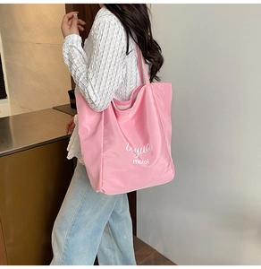 Side view of a large pink nylon tote bag with white lettering worn by a female model