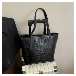 Detail of black faux crocodile leather tote bag with embossed crocodile head on a suitcase