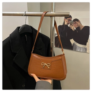 Détail d'un sac à main marron motif crocodile avec nœud doré métallique