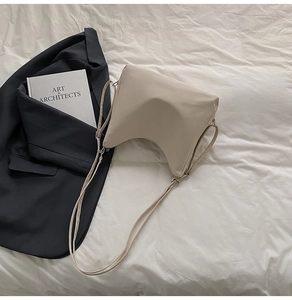 Detail view of a beige minimalist crossbody bag with curved bottom on a fabric background