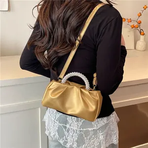 Gold pleated dumpling bag with pearl handle and shoulder strap worn by a model