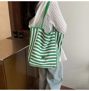 Detail of green and white striped knit tote bag with a vintage oval bronze logo plaque