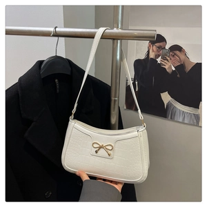 Détail du sac baguette blanc à motif crocodile avec une boucle en nœud doré élégante